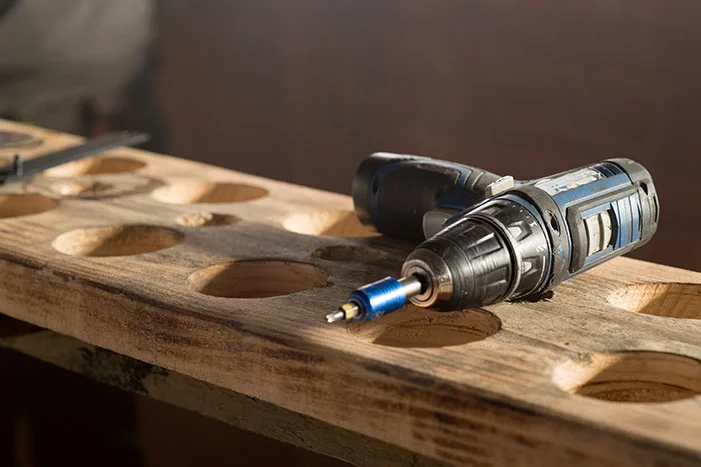 Ein Akkuschrauber liegt auf einem Holzbrett mit vorgebohrten Löchern.